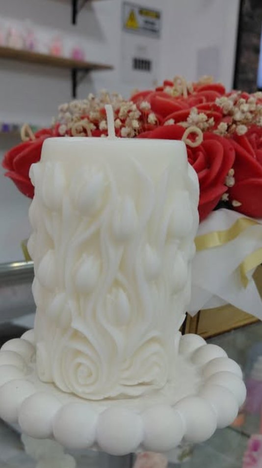 Vela tallada con tulipanes junto a rosas de cera rojas